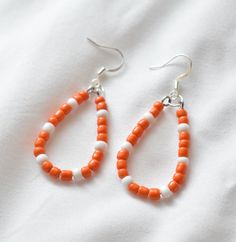 These handmade orange and white beaded earrings are the perfect addition to any outfit. They are lightweight, comfortable, and made of hypoallergenic materials.  2.5 inches in length. You have the option of gold- or silver-colored ear hooks. Care Instructions: - Keep away from moisture - Remove when sleeping - Remove before entering water - Store in cool dry area - Gently wipe with soft cloth to clean These unique handmade earrings would make the perfect birthday gift, anniversary gift, bridesmaid gift, Christmas gift, Valentines day gift, mothers day gift, teacher gift, gift for her, and so much more!  Thank you so much for checking out my shop! Don't hesitate to message me with any questions!  - Tennessee Earrings, TN Jewelry, TN Vols Earrings, Tennessee State Colors, Tennessee Vols Earr White Teardrop Beaded Earrings For Beach, Orange Teardrop Beaded Earrings As Gift, Orange Teardrop Beaded Earrings For Gift, Orange Teardrop Beaded Earrings With Ear Wire, Orange Teardrop Beaded Earrings, Orange Teardrop Beaded Earrings With Dangling Beads, White Teardrop Beaded Earrings For Pierced Ears, Orange Teardrop Earrings With Dangling Beads, White Teardrop Beaded Earrings