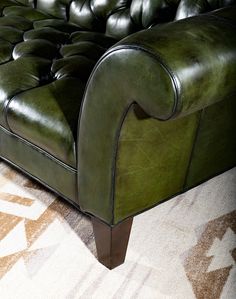 a green leather couch sitting on top of a carpeted floor next to a rug