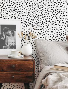 a bedroom with black and white polka dot wallpaper, a coffee cup on a dresser next to the bed