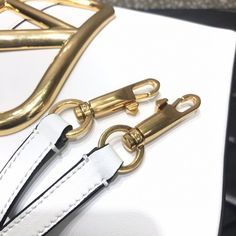 a white purse with gold hardware and leather straps on it's side, sitting on a table