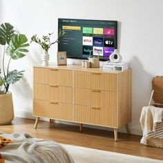 a flat screen tv sitting on top of a wooden dresser in a living room next to a potted plant