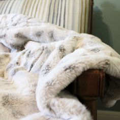 a couch covered in white fur with a wooden arm rest and striped pillow behind it