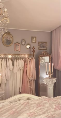 a room with a bed, chandelier and dresses hanging on the rack in it