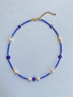 Protect yourself in style with our stunning Evil Eye beaded necklace. This piece combines the mystical charm of the evil eye symbol with the elegance of freshwater pearls and the vibrant beauty of blue seed beads and gold beads. Crafted with durable stainless steel, this necklace is both waterproof and tarnish-resistant, ensuring lasting beauty and protection. Key Features: Evil Eye Charm: Symbolizing protection and warding off negativity, the evil eye charm adds a meaningful touch to this beautiful necklace. Freshwater Pearls: Genuine freshwater pearls provide an elegant and timeless appeal. Blue Seed Beads: Vibrant blue seed beads enhance the necklace's aesthetic and add a pop of color. Gold Beads: High-quality gold beads offer a luxurious touch. Stainless Steel: Made with durable stainl White Evil Eye Beaded Necklace, Handmade Pearl Beaded Necklaces For Festivals, Handmade Pearl Beaded Necklace For Festivals, Blue Pearl Jewelry With Colorful Beads, Blue Bohemian Pearl Necklaces, Bohemian Blue Pearl Jewelry, Blue Bohemian Pearl Necklace, Adjustable Beads With Pearl Charm, Handmade Adjustable Pearl Beads