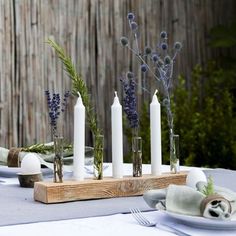 the table is set with white candles and blue flowers in glass vases on wooden stand