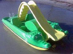 a green toy boat with an alligator on it's side in the water at the beach