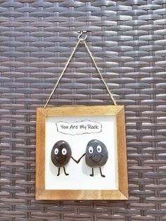 two black rocks hanging from a wooden frame on a wicker wall with the words you are my rock written above them