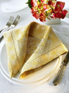 a white plate topped with two yellow napkins next to a vase filled with flowers