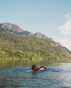 a man swimming in the middle of a lake with mountains in the backgroud