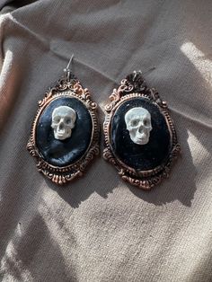 Add a touch of macabre elegance to your Halloween ensemble or any outfit with a dark, mysterious flair with these handcrafted Framed Skull Earrings. Made from durable and lightweight polymer clay, these earrings are designed to withstand wear and tear, making them a great choice for everyday wear. The meticulously sculpted skull centerpiece is set within a detailed copper frame, adding a unique and intricate design element to the earrings. The copper frame is aged with black paint, giving the earrings a vintage and rustic look that complements the gothic-inspired design. The earrings are cured with a water-based clay top coat, ensuring that the colors and details of the design are long-lasting and won't fade or wear off easily. The black paint used in the aging process adds depth and dimen Skull Centerpiece, Dark Mysterious, Copper Frame, Gothic Skull, Halloween Outfit, Skull Earrings, Intricate Design, Looks Vintage, Black Paint