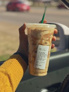 a person holding up a cup with a green straw in it's hand while driving