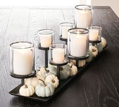 candles are arranged on a black tray with white pumpkins