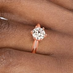 a woman's hand with a rose gold ring on her finger and a white diamond in the middle