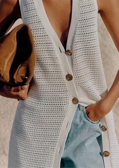 a woman is wearing a white vest and holding a brown hat