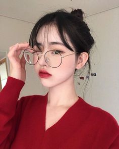 a woman wearing glasses and a red sweater is holding her hair in one hand while looking at the camera