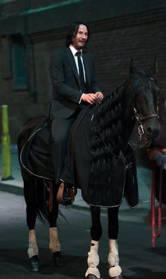 a man riding on the back of a black horse next to a person in a suit