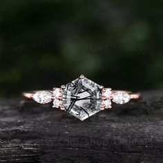 an engagement ring with three stone accents on top of a piece of wood in front of trees