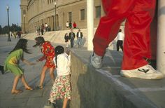 several children are playing on the sidewalk in front of a large statue