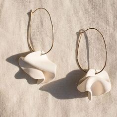 two white flower shaped earrings sitting on top of a cloth covered table next to a pair of gold hoop earrings