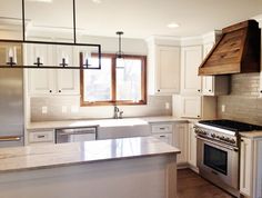 a kitchen with white cabinets and stainless steel appliances, including an oven, range hood, dishwasher, sink, and refrigerator