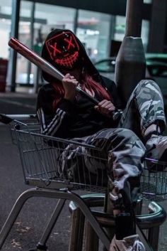 a person sitting in a shopping cart wearing a mask and holding a baseball bat with both hands