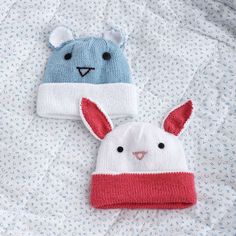 two knitted animal hats laying on top of a bed covered in blue and white sheets