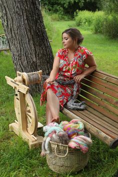 a woman sitting on a bench next to a basket with yarn and a spinning wheel