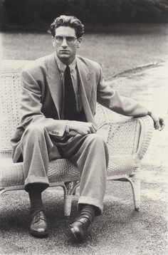 black and white photograph of a man in suit sitting on a wicker chair with his legs crossed