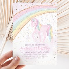 a hand holding up a birthday card with a unicorn on it and a rainbow in the background