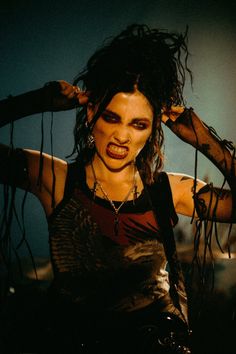 a woman with long hair and black makeup is posing for the camera while holding her hands behind her head