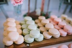 macaroons are arranged in rows on a wooden platter next to a vase with pink flowers