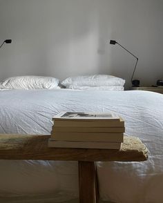 a stack of books sitting on top of a wooden table next to a white bed