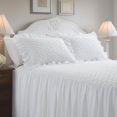 a white bed with three lamps on either side and two pictures above the headboard