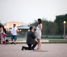 a man kneeling down next to a woman on top of a brick floor near other people