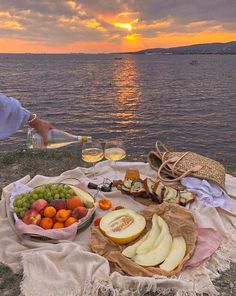 a person sitting on a blanket near the water with food and wine in front of them