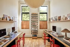 an office with two desks and red chairs in front of a wall mounted bookshelf