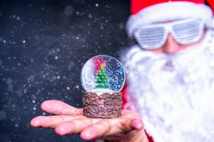 santa claus holding up a snow globe with a christmas tree in it's palm