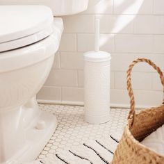 a white toilet sitting next to a wicker basket on top of a bathroom floor