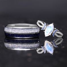 two rings with blue and white stones on them sitting next to each other in front of a reflective surface