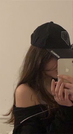 a woman wearing a black hat and holding an iphone in her right hand while looking at the camera