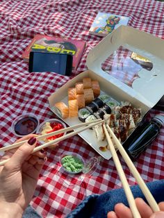 someone is eating sushi and chopsticks at a picnic table with a red checkered cloth