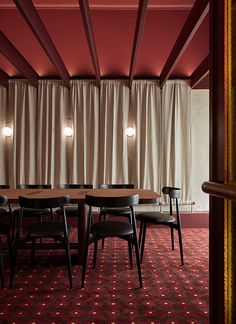 a dining room with red walls and wooden table surrounded by black chairs in front of a curtained wall