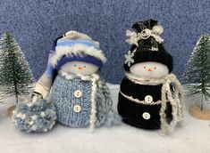 two knitted snowmen standing next to each other in front of small christmas trees