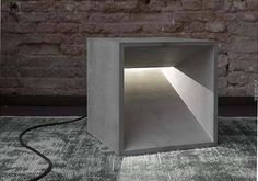 an empty concrete box sitting in front of a brick wall with a light coming through it