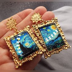 a pair of earrings with the starry night painting on them is being held in someone's hand