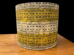 a yellow and white patterned lamp shade sitting on top of a wooden table next to a black wall