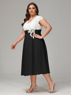 a woman wearing a black and white dress with flowers on the waist, standing in front of a gray background