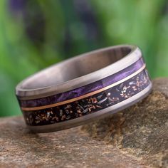 a wedding band with purple and gold inlays sits on top of a rock