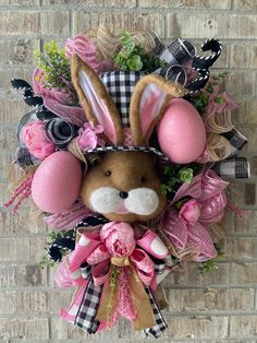 a bunny wreath hanging on a brick wall with pink eggs and flowers in it's ears