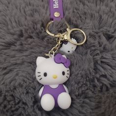 a hello kitty keychain with a purple bow on it's head sitting on a furry surface